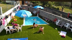 Un patio trasero con piscina, rodeado de césped artificial y varias sillas y sombrillas de plástico.