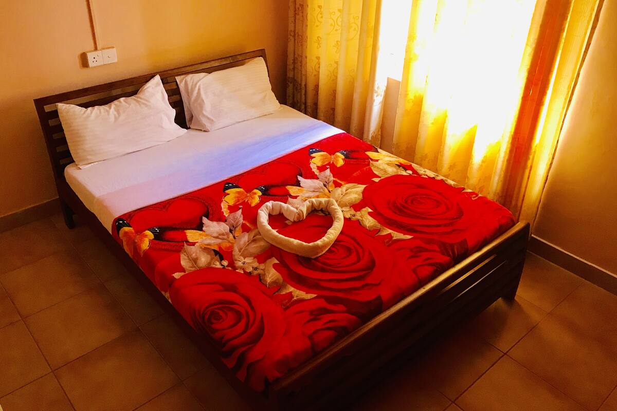 Una cama con una colcha estampada con flores, almohadas blancas y una decoración con forma de corazón.
