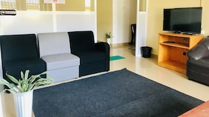A living room with a sofa, a television on a wooden stand, a potted plant, and a calendar on the wall. - Casablanka Rest (Nanuoya)