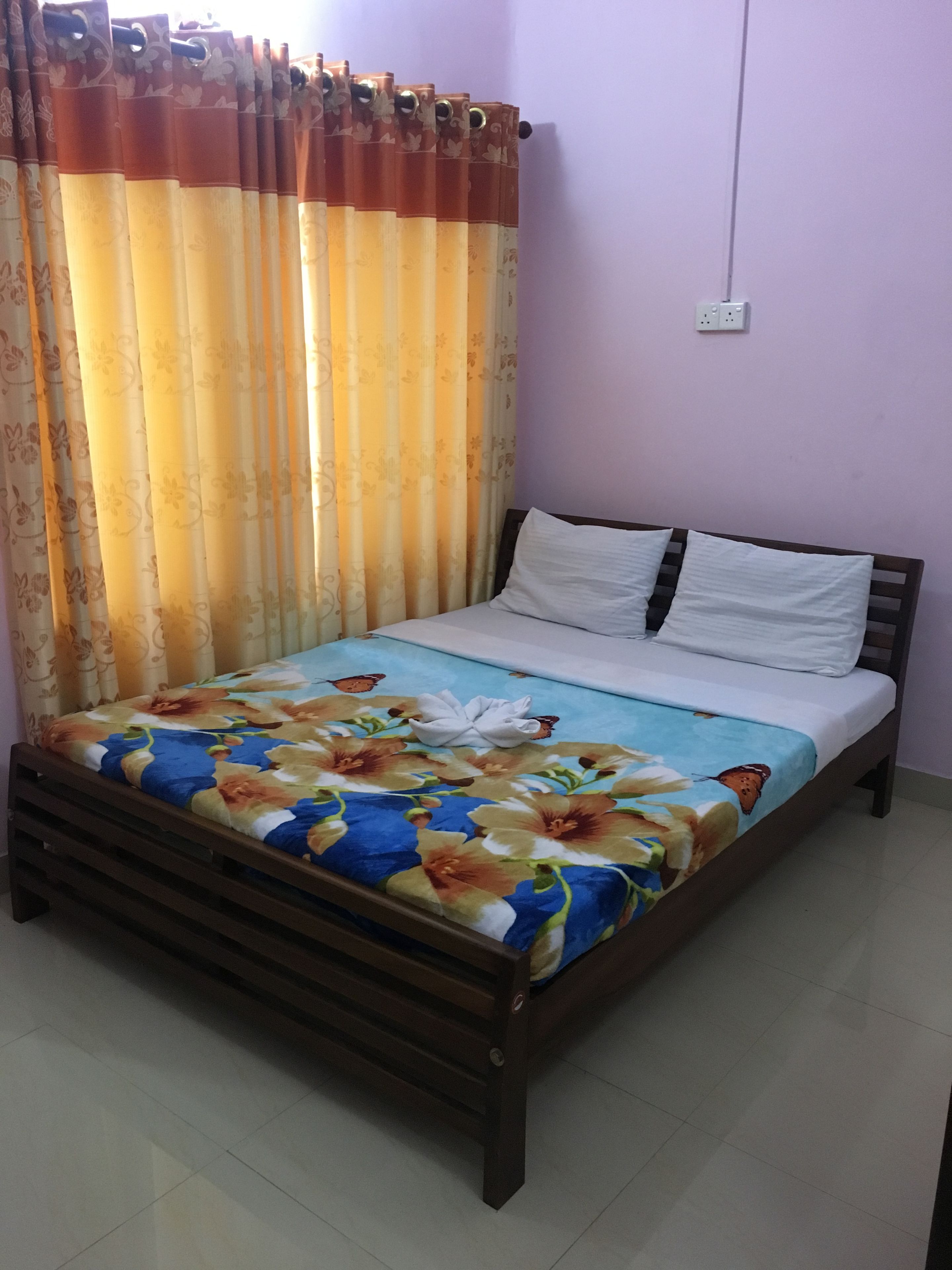 A bedroom with a bed, curtains, and a wall socket.