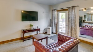 Un salon avec un canapé en cuir, un téléviseur fixé au mur, une petite table et une fenêtre avec des rideaux.