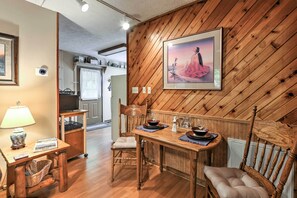 Un coin repas avec une table et des chaises en bois, un tableau encadré au mur et une lampe sur une table d’appoint.