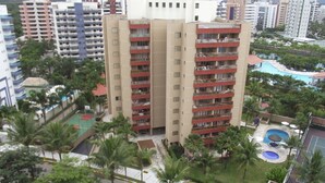 A high-rise building with multiple balconies, surrounded by palm trees and a swimming pool area. - Riviera apartment, 50m from the beach 3 bedrooms 2bh, living room 2 rooms, balcony, air conditioning, wi-fi  (Bertioga)