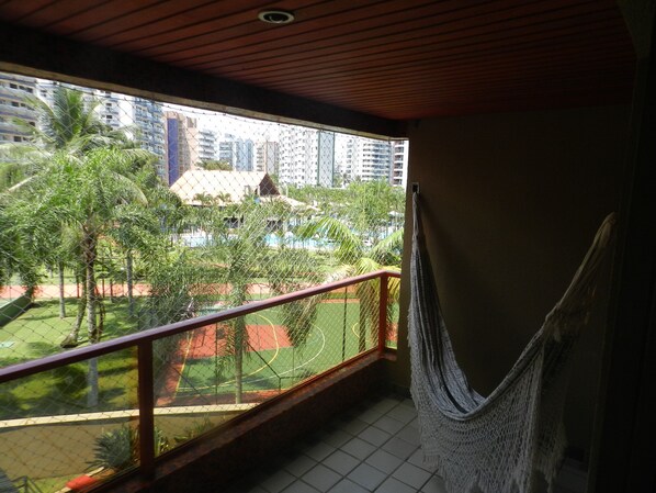 A balcony with a hammock, a view of a sports court, and a building in the background. - Riviera apartment, 50m from the beach 3 bedrooms 2bh, living room 2 rooms, balcony, air conditioning, wi-fi (Bertioga)