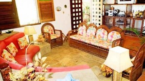 A living room with a red sofa, a wooden bench with floral cushions, a coffee table with a lamp, and a television on the wall.