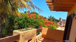 A balcony with a view of a garden, a chair, and a potted plant.
