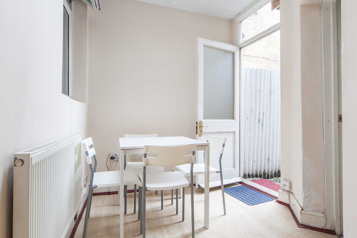 A small, bright room with a white table and chairs, a radiator, and a window with blinds.