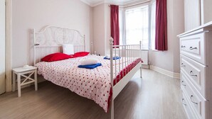 Une chambre à coucher avec un lit en métal blanc, une table de chevet blanche et une commode blanche.