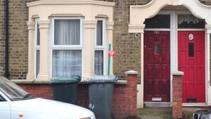 Une maison à deux étages avec une porte rouge et une fenêtre au-dessus de laquelle est accrochée une enseigne.