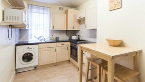 Une cuisine compacte avec des meubles de rangement en bois, un lave-linge, une cuisinière et une table en bois.