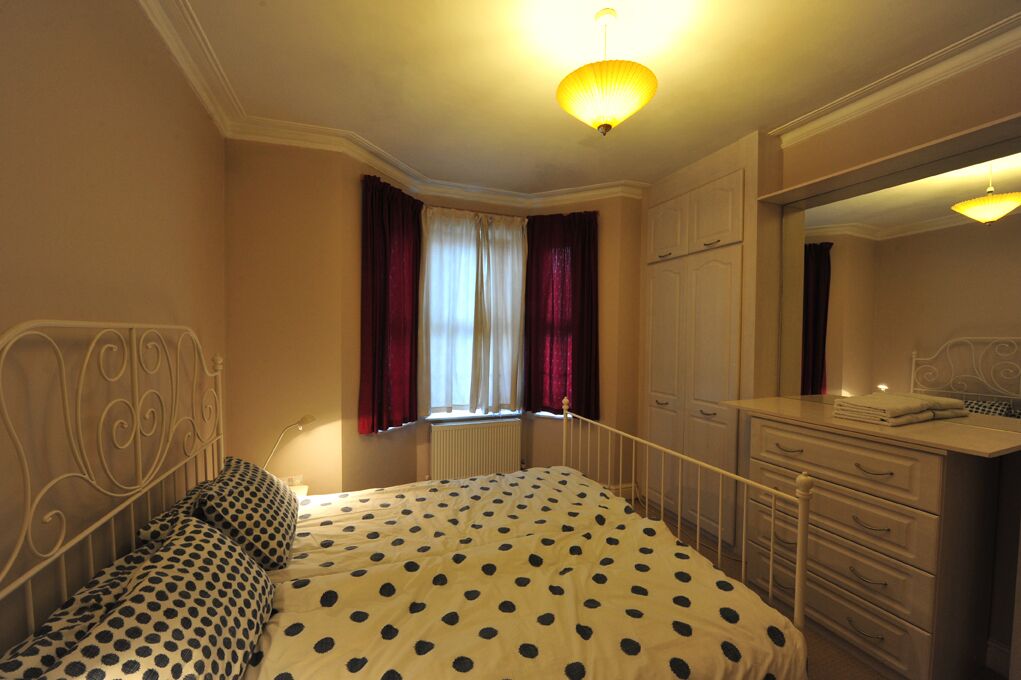 Une chambre à coucher avec un lit, une commode, un miroir et une fenêtre avec des rideaux.