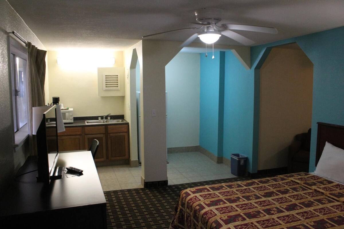 Une chambre d’hôtel équipée d’un lit, d’un bureau, d’une kitchenette et d’un ventilateur de plafond.