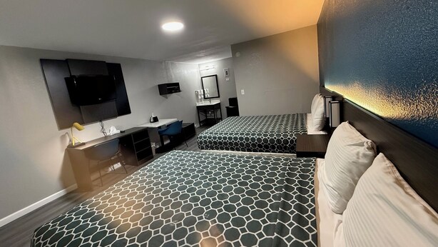 Habitació d'hotel amb dos llits, un escriptori, un televisor, un mirall i un bany.