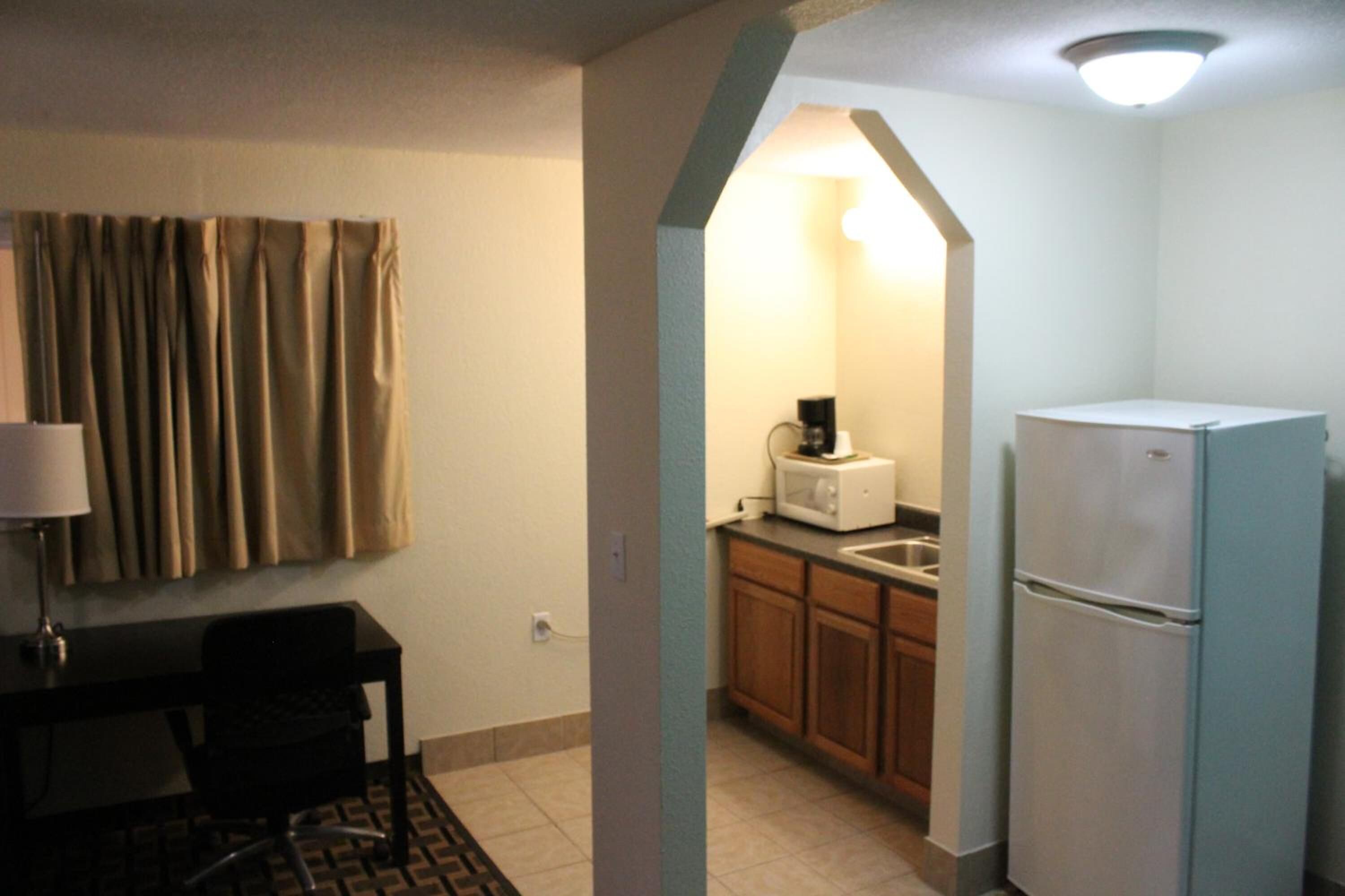 Cocina compacta con refrigerador, microondas y lavamanos. Hay una zona de comedor con mesa y sillas.
