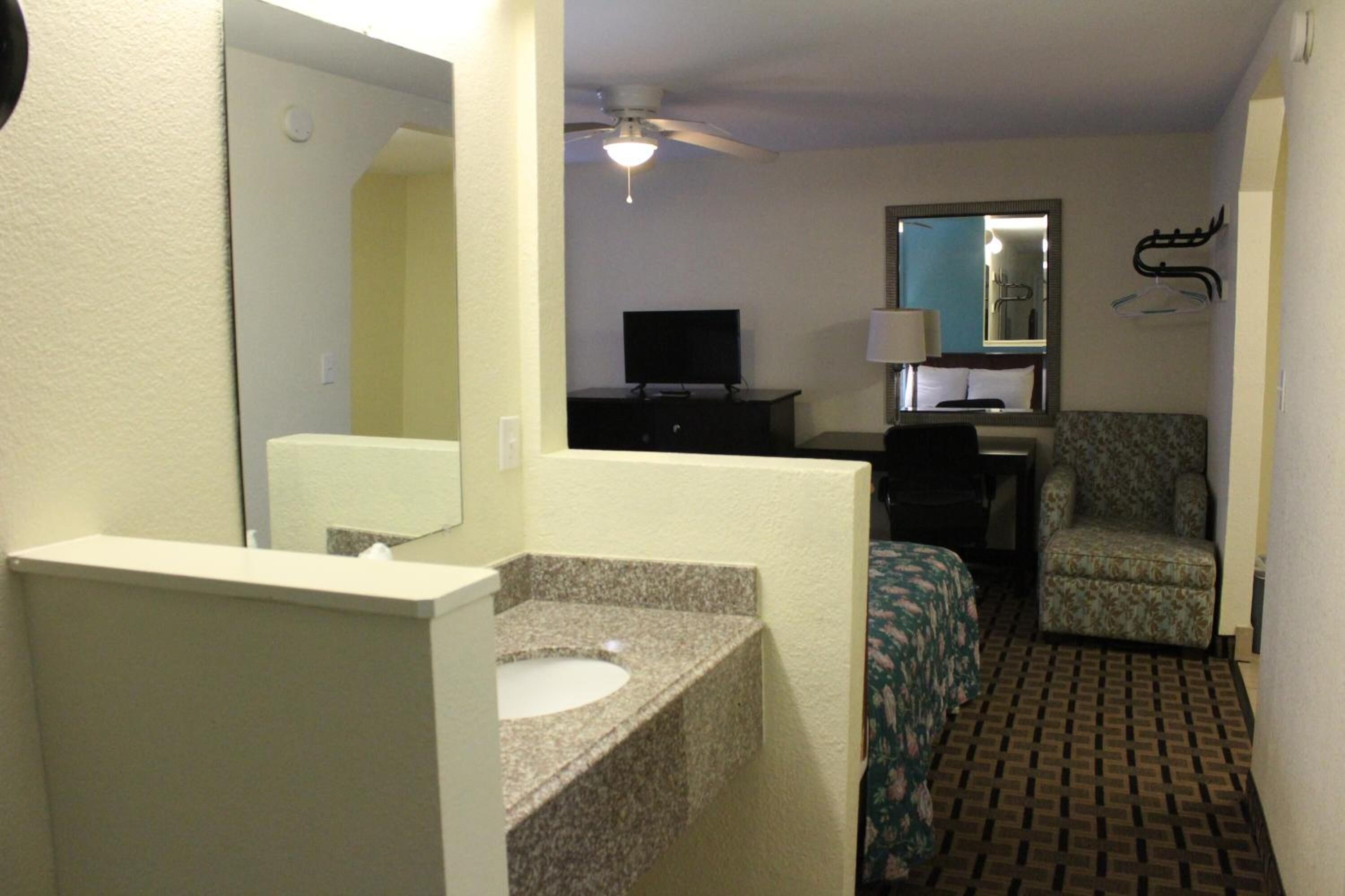 A small, compact hotel room with a bathroom, a bed, a television, and a chair.