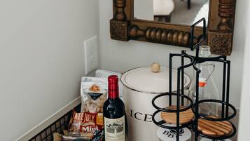 A kitchen counter with a wine bottle, a coffee maker, a basket of snacks, and a milk jug.