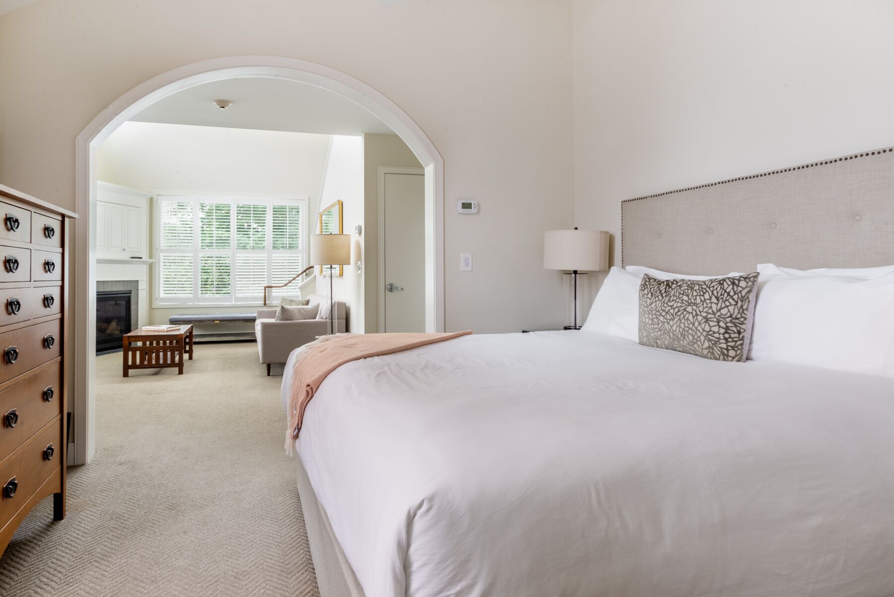 Habitación de hotel con una cama grande, un escritorio y una silla. Hay una chimenea, una ventana con persianas y una puerta que conduce a otra habitación.