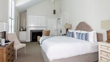 A bedroom with a large bed, a chair, a dresser, a fireplace, and a ceiling fan.