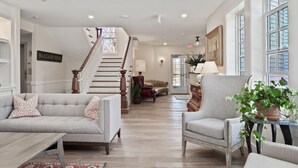 Un salón amplio con escaleras, un conjunto de sofás y un gran ventanal.