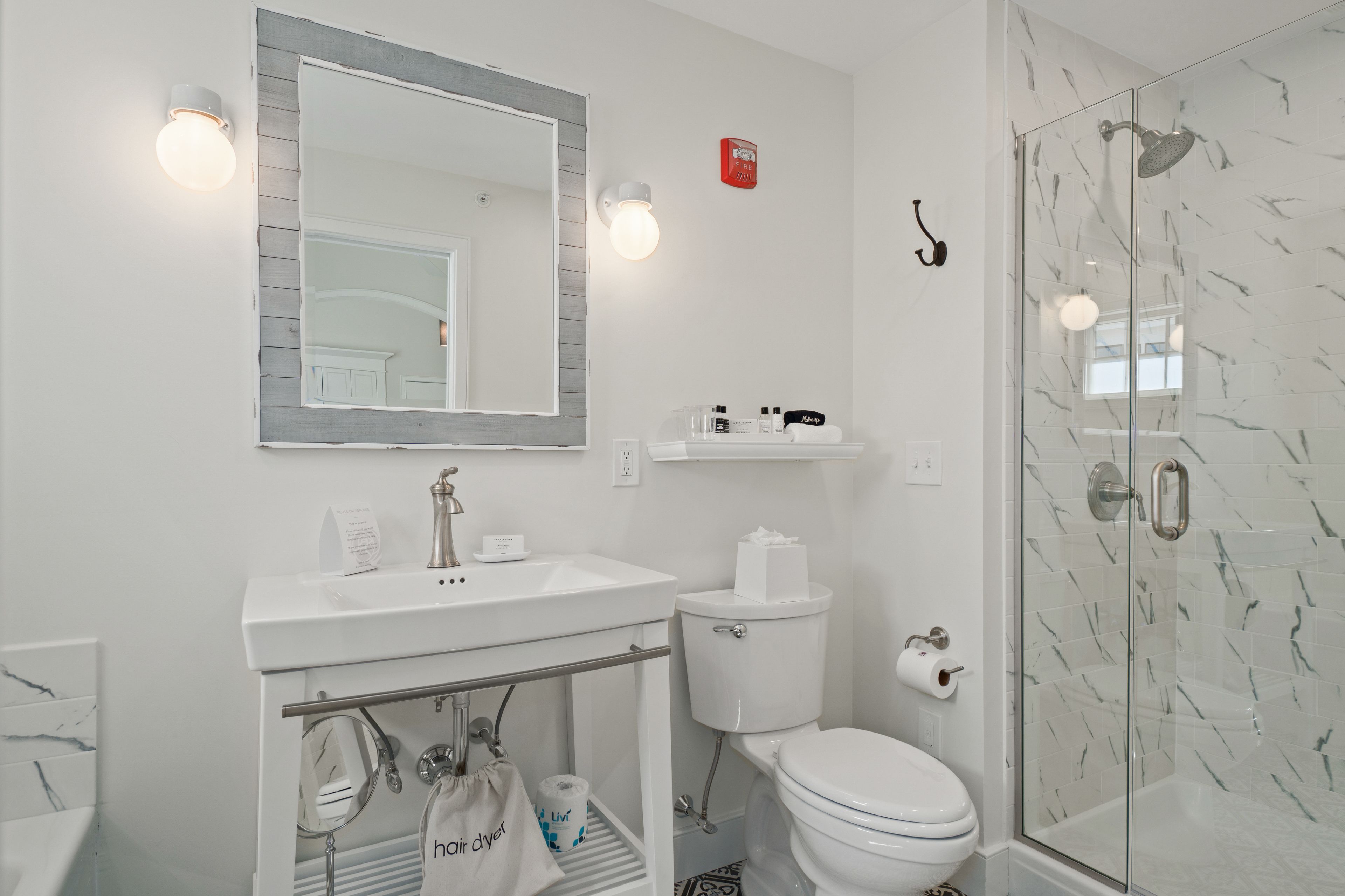 A modern bathroom with a white sink, mirror, and toilet. There is a glass shower enclosure with a showerhead.