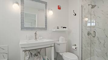 A modern bathroom with a white sink, mirror, and toilet. There is a glass shower enclosure with a showerhead.