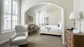 Habitación de hotel con cama, escritorio, silla, cómoda y un amplio ventanal con persianas.