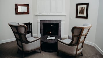 A room with a fireplace, two armchairs, a small round table, and a mirror on the wall.