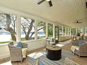 A covered patio with wicker furniture, a round coffee table, and large windows overlooking a river. - LOCATION!! Lake Travis Waterfront~Pool, Spa, Outdoor Kitchen, Location (Austin)