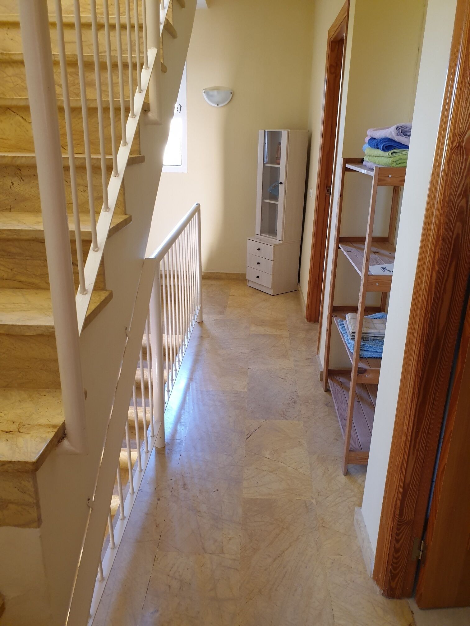 A staircase with white railings leading to a landing. There is a wooden cabinet with drawers and a glass-fronted cabinet on the landing.