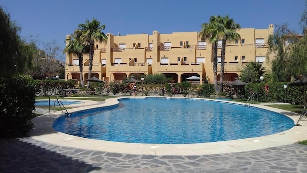A swimming pool surrounded by palm trees and a building with multiple balconies. - House (triplex) in Puerto Rey, Vera Playa, Almeria, 400m from beach (Puerto Rey, Vera Playa)
