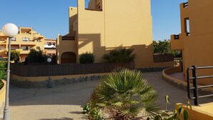 A building with a flat roof and a balcony, surrounded by a paved courtyard with palm trees and a stone wall. - House (triplex) in Puerto Rey, Vera Playa, Almeria, 400m from beach (Puerto Rey, Vera Playa)