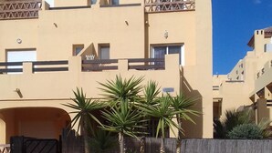 A building with a beige facade, a gated entrance, and a paved courtyard with palm trees. - House (triplex) in Puerto Rey, Vera Playa, Almeria, 400m from beach (Puerto Rey, Vera Playa)