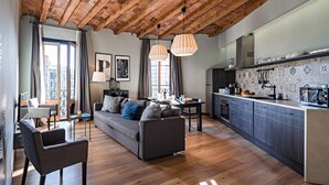A modern living room with a sofa, chairs, and a dining area. There is a kitchen with a tiled backsplash and wooden cabinets.