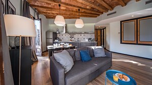 A modern living room with a grey sofa, a blue side table with croissants, and a kitchen in the background.