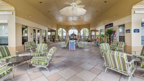A covered outdoor seating area with striped chairs and tables, a central flower arrangement, and signs for amenities like a spa and restaurant. - Disney Magic Awaits: 5-BDRM, 3-Suites, Pool, Upgraded Perks,  and Tile Flooring! (Kissimmee)