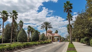 A well-maintained road with a clear sky, palm trees, and a building with a red roof. - Disney Magic Awaits: 5-BDRM, 3-Suites, Pool, Upgraded Perks,  and Tile Flooring! (Kissimmee)