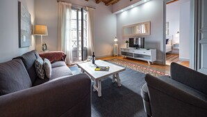 Ein modernes Wohnzimmer mit einer Couch, einem Couchtisch, einem Fernseher und einem großen Fenster mit Vorhängen.