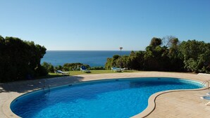 A swimming pool with a curved edge, surrounded by a paved deck and lounge chairs. - Charming villa, beautiful sea view. Swimming pools. Sand beach. Very calm. (Porches)