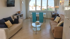 A living room with two sofas, a coffee table, a TV mounted on the wall, a dining area with a table and chairs, and a view of the sea through large windows. - Charming villa, beautiful sea view. Swimming pools. Sand beach. Very calm. (Porches)