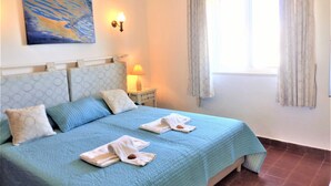 A bedroom with a bed, pillows, a bedside table with a lamp, a painting on the wall, and a window with curtains. - Charming villa, beautiful sea view. Swimming pools. Sand beach. Very calm. (Porches)