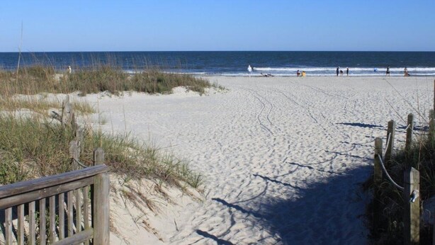Ein Sandstrand mit einer Holzumzäunung und freiem Blick auf den Ozean.