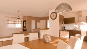 Una cucina moderna con elettrodomestici integrati, un'area pranzo con tavolo in legno e sedie bianche, e un grande vaso decorativo sul tavolo.