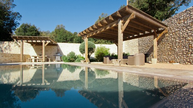 Una piscina limpida con pergole in legno e pareti in pietra.