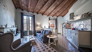 Una sala acogedora con un sofá, sillas, una mesita redonda y una cocina con armarios y una encimera.