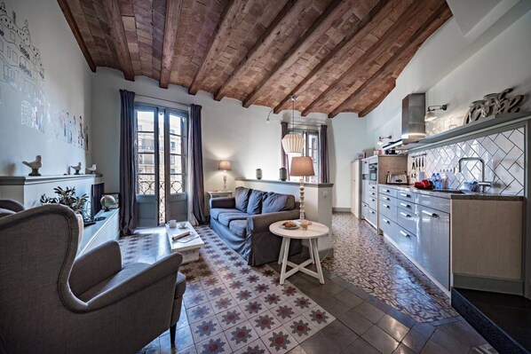 A cozy living room with a sofa, a dining table, and a kitchen area with cabinets and a countertop.