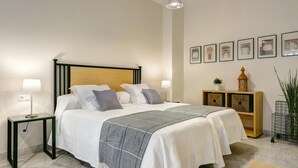 A neatly arranged bedroom with a bed, bedside lamps, a nightstand, a bedside table, a wooden nightstand, a wall-mounted shelf, and framed pictures. - Genteel Home Tomas de Ibarra (Sevilla)