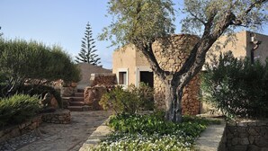 Um edifício de pedra com porta e janelas, rodeado por um caminho de pedra e vegetação.