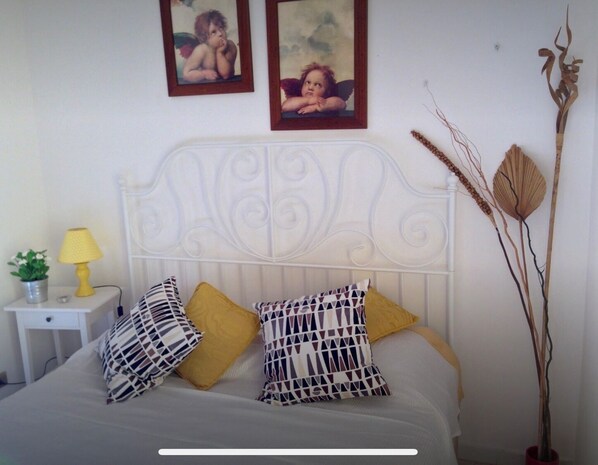 A bedroom with a white headboard, two pillows, a bedside table with a lamp, and a wall-mounted picture. - Robi Mare San Pietro house (Ladispoli)