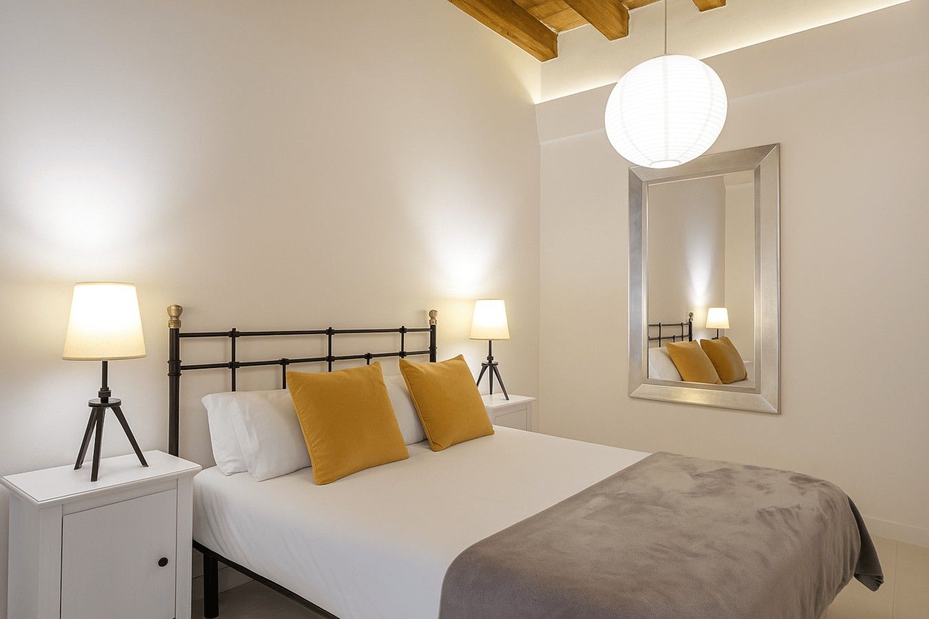 Una habitación de hotel con una cama, dos mesitas de noche, lámparas, un espejo y una lámpara en el techo.
