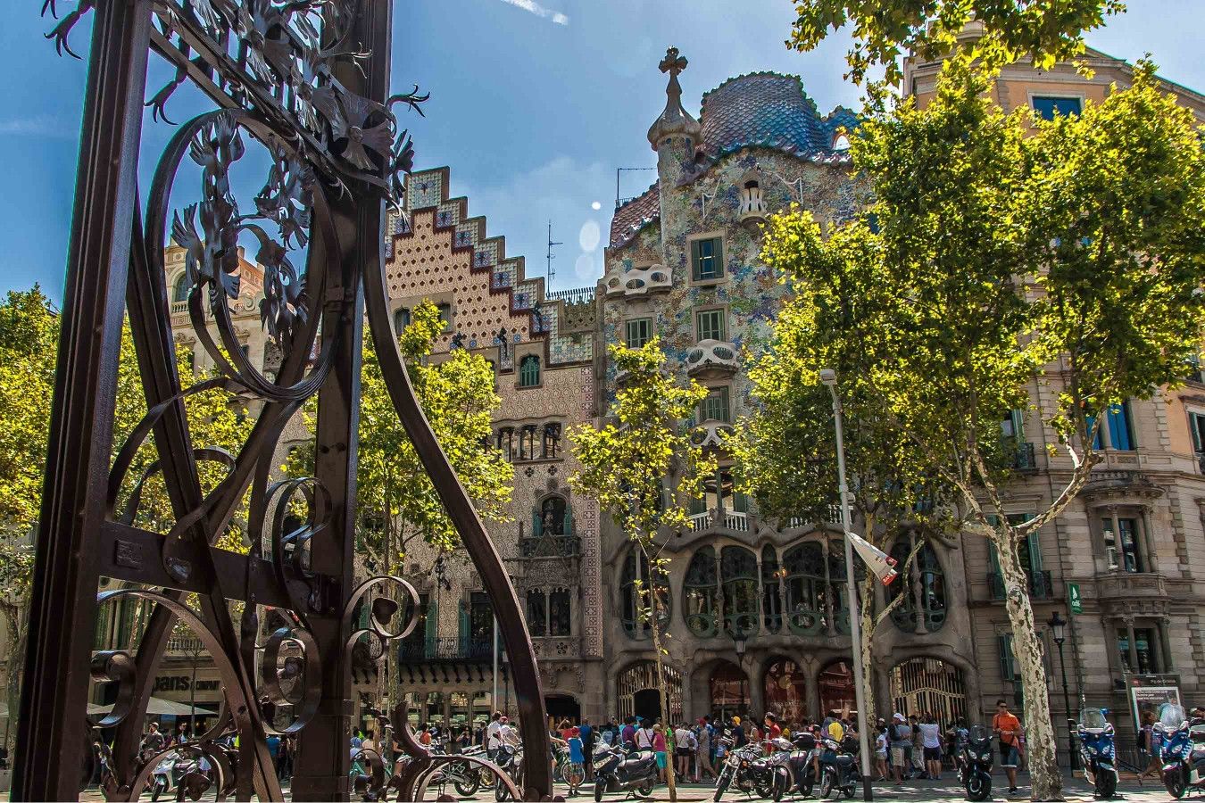 Un edificio histórico con arquitectura detallada, una plaza pública con árboles y una multitud de personas.